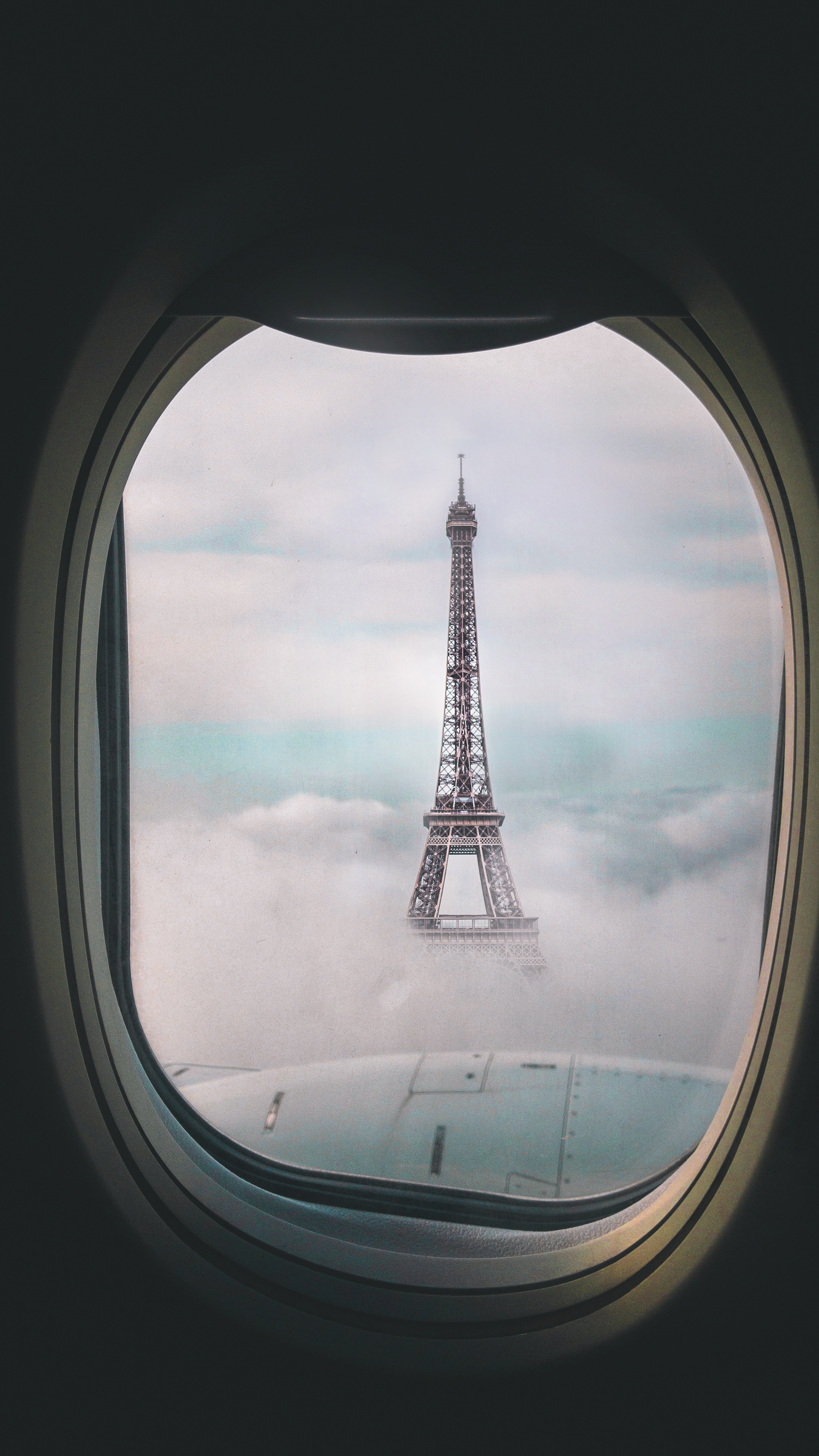 The Eiffel Tower poking through the clouds behind an airplane window